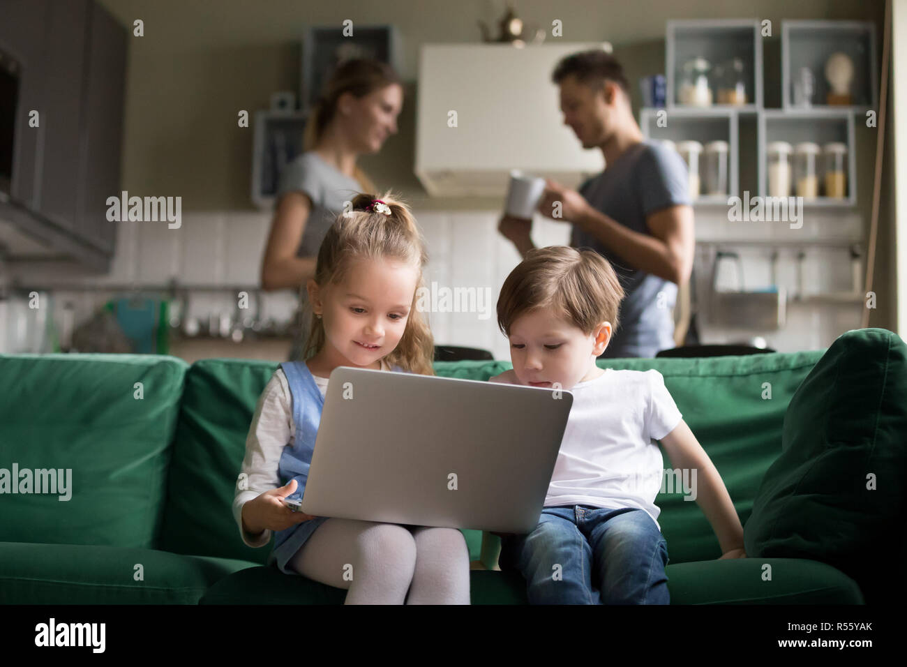 Little girl and boy using laptop while parents en parler Banque D'Images