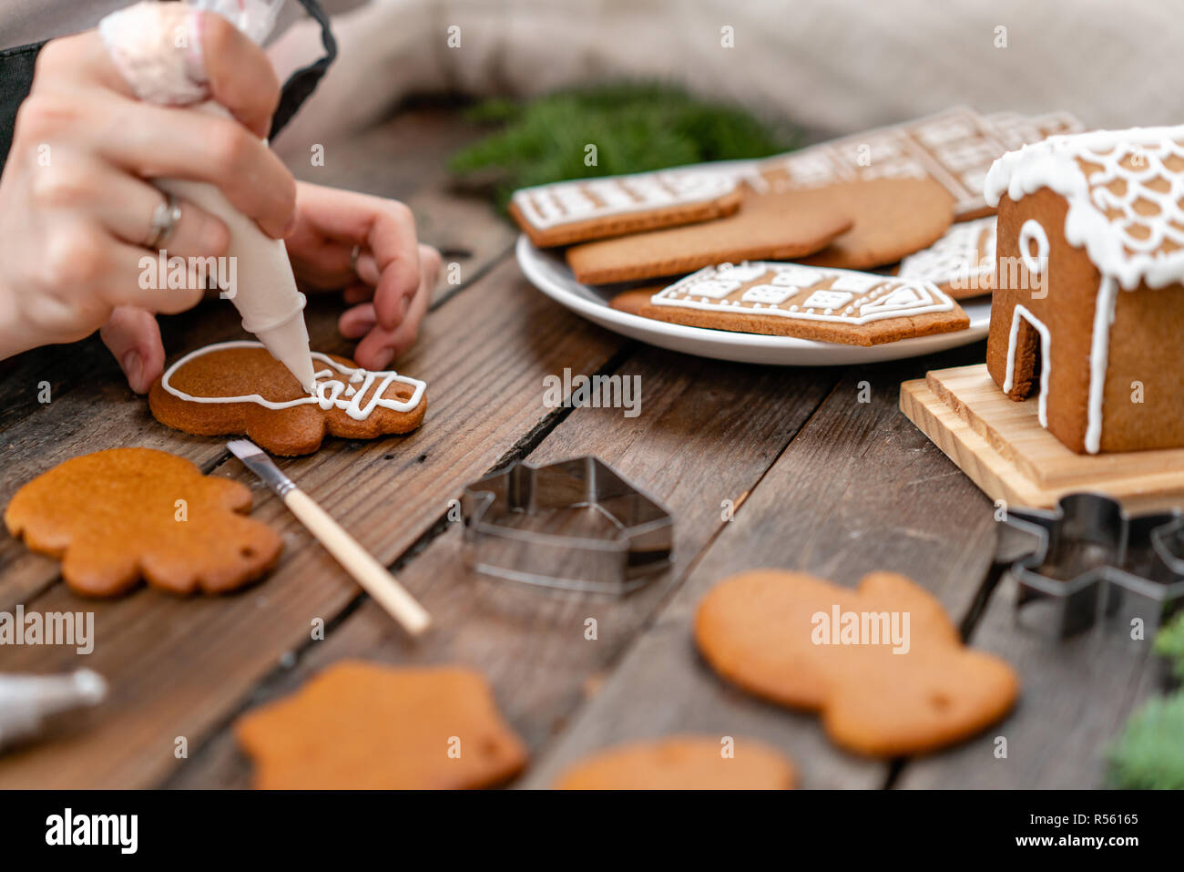 Une jeune fille décore ginger cookies sous la forme d'hiver Noël Bonhomme de matin. Cerise sur le miel attire femme gingerbread cookies. Table marron en bois. copier l'espace. Banque D'Images