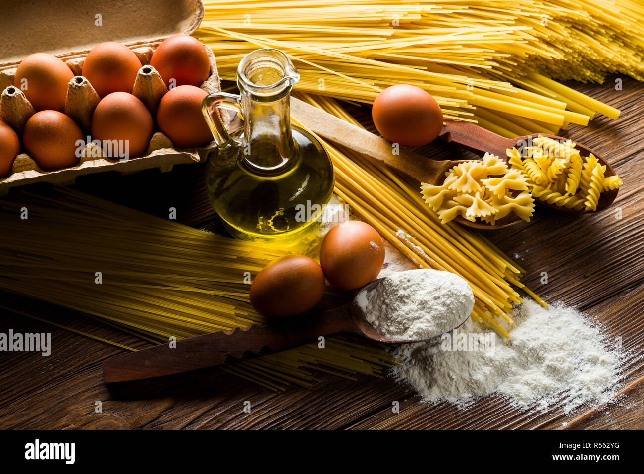 Spaghettis et pâtes alimentaires non cuites sur une table avec des œufs et de la farine et d'huile d'olive Banque D'Images