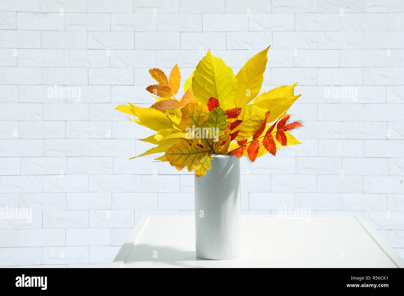 Un bouquet de feuilles d'automne dans un vase blanc à l'intérieur. Arrière-plan en brique blanche. Banque D'Images