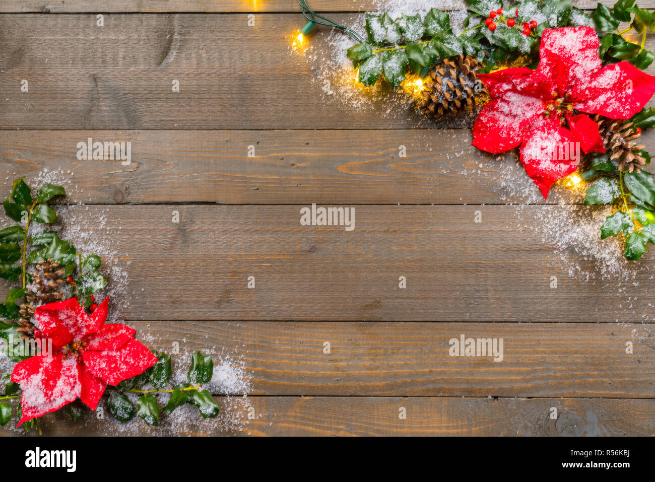 Houx de Noël avec de la neige, poinsettia, lumières et les baies sur un fond de bois Banque D'Images