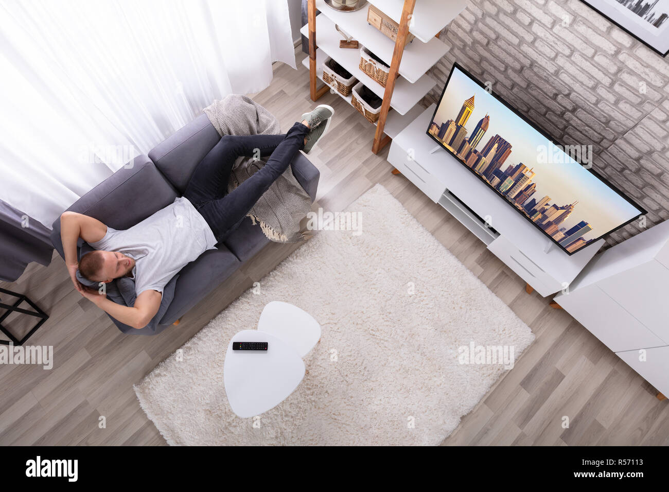 High Angle View of a Young Man Relaxing On Sofa Watching Television Banque D'Images