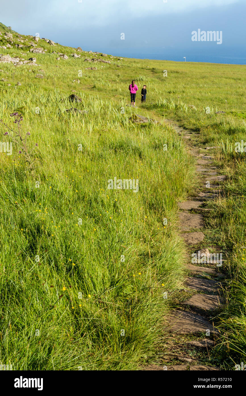 Fille et garçon debout et le chat à la fin d'un sentier rocailleux, Garrafad, île de Skye, Hébrides intérieures, Ecosse, Royaume-Uni Banque D'Images