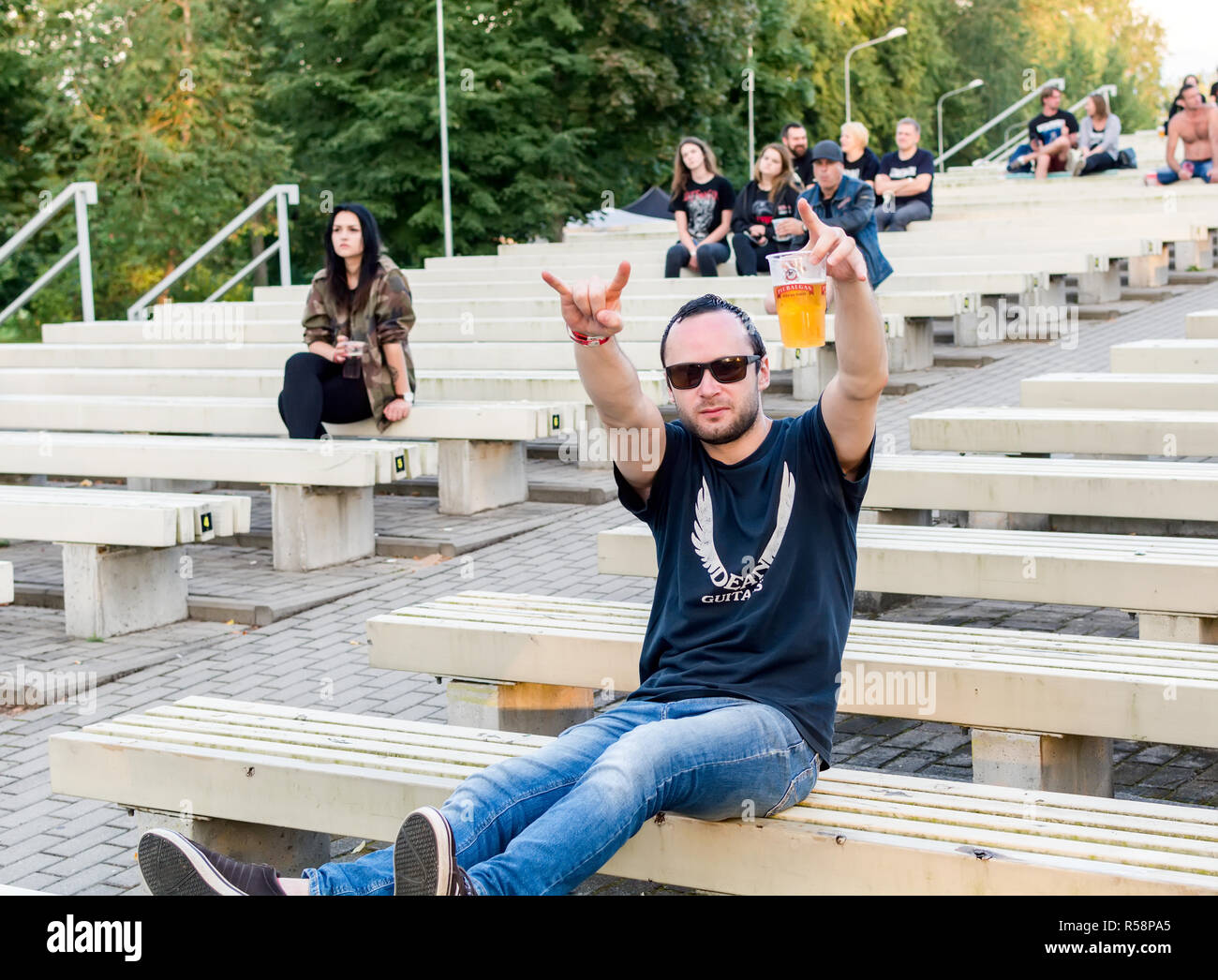 Fan de heavy metal assis dans les gradins avec tasse de bière dans une main et montrant les cornes de signer avec un autre à Metalshow Open Air festival en Lettonie Banque D'Images