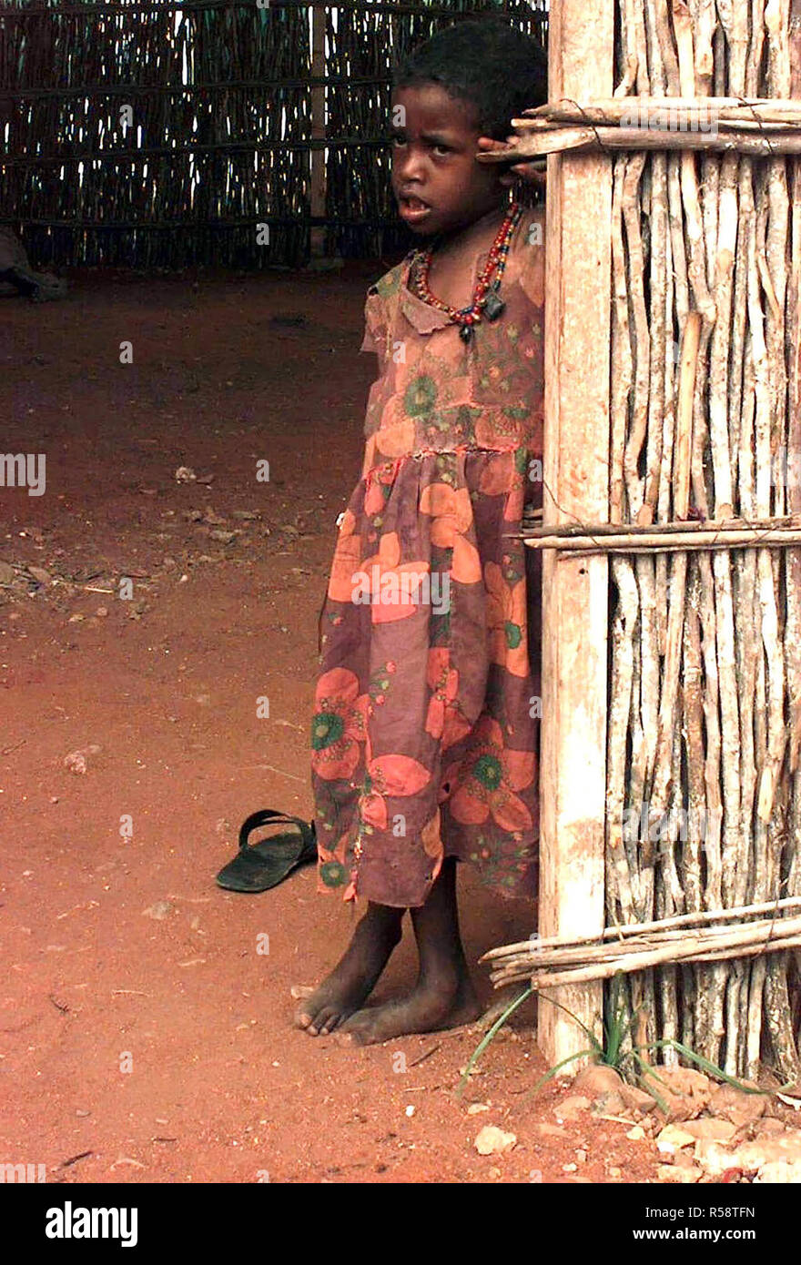 1992 - tout droit, medium close-up d'une petite fille somalienne, environ six ou sept ans. Elle porte une robe à fleurs et s'appuie contre l'entrée d'une cabane en bambou avec un plancher en terre battue. Banque D'Images
