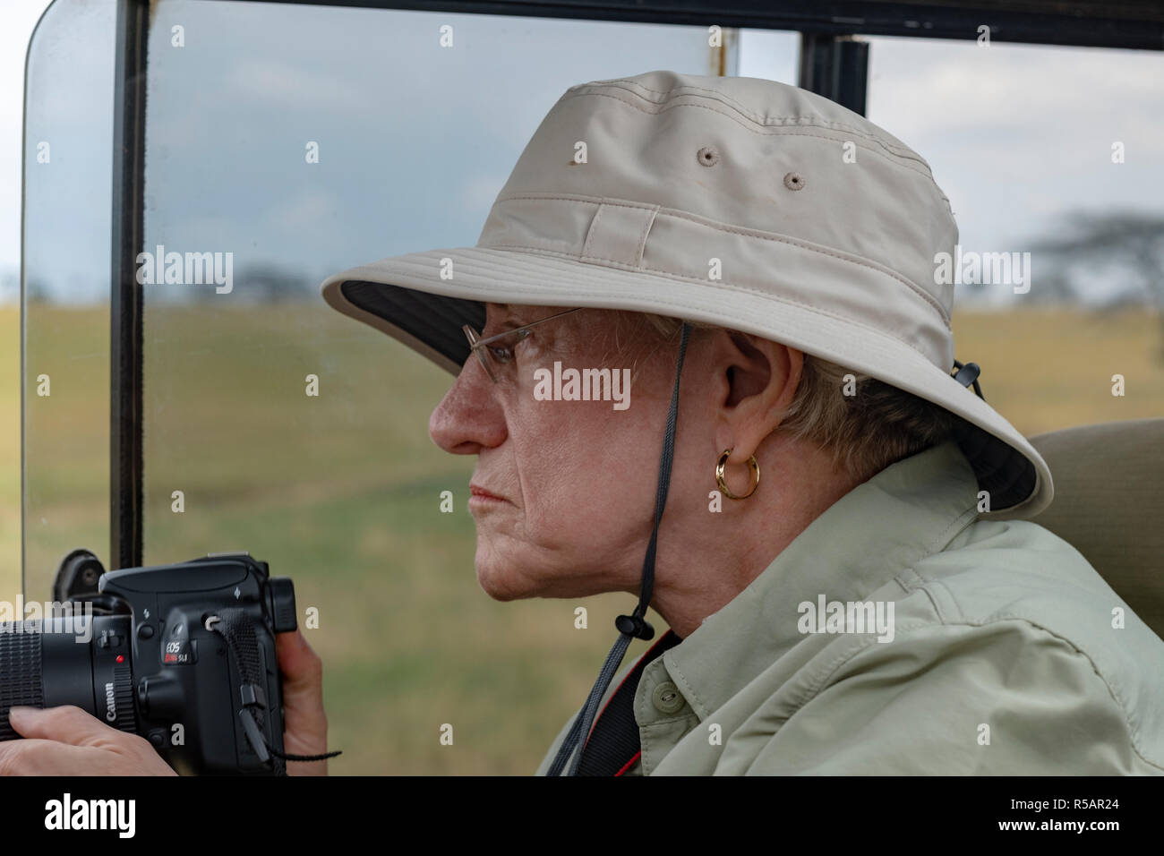 Femme plus âgée bénéficie d'un safari-photo en Tanzanie en photographiant la faune d'un Land Rover dans le Parc National de Serengetti Banque D'Images