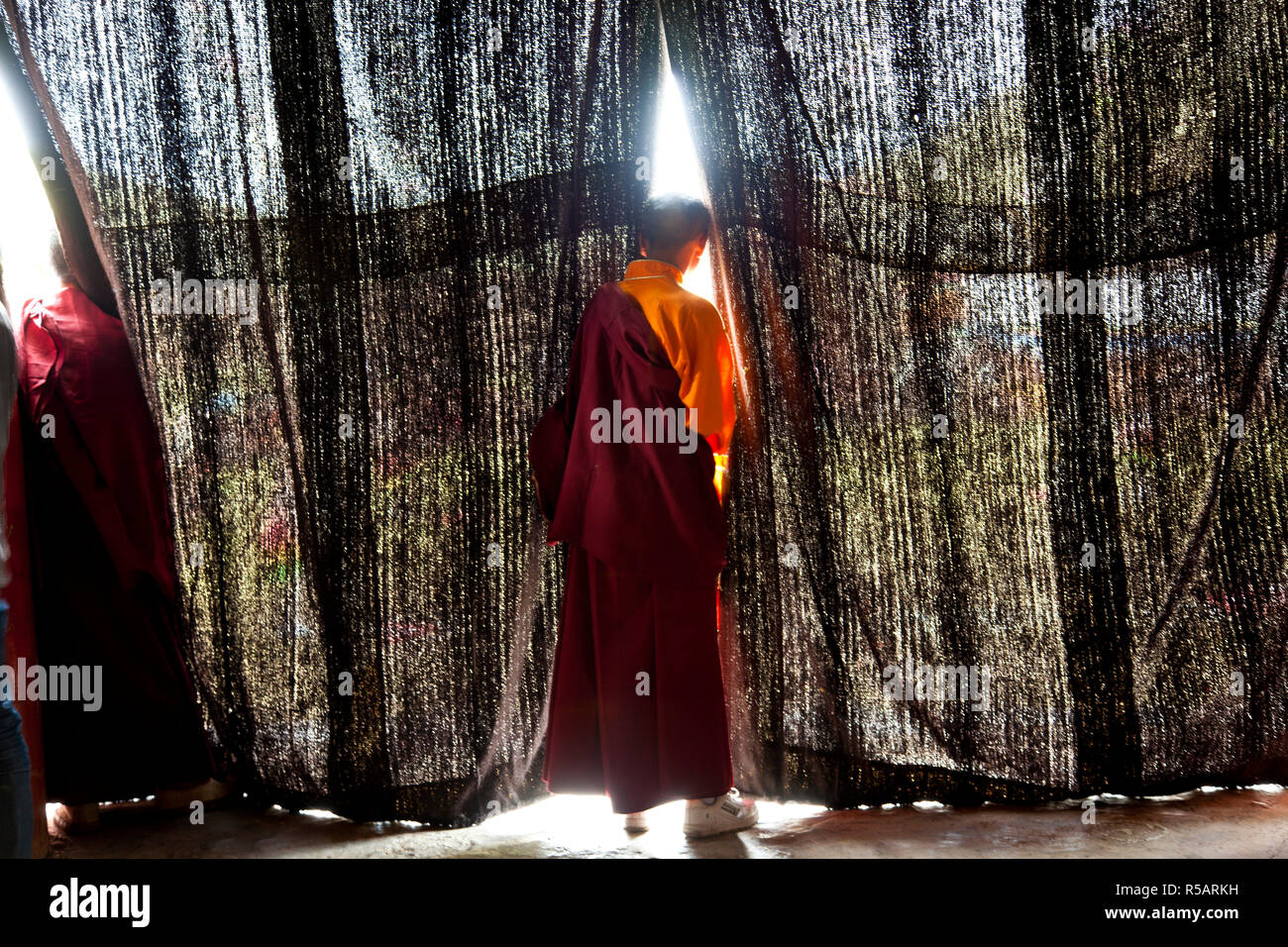Les jeunes moines à la recherche à travers les rideaux à festival danse masquée au Keno Gompa ou monastère, Tagong, région tibétaine du Sichuan, Chine ; Banque D'Images