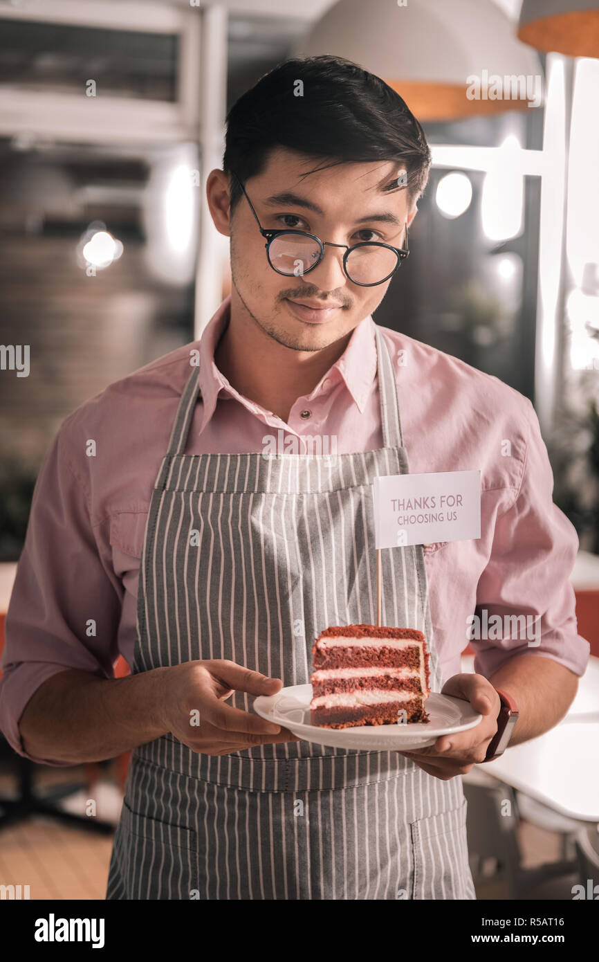 Handsome man wearing glasses holding cake de son cafe Banque D'Images