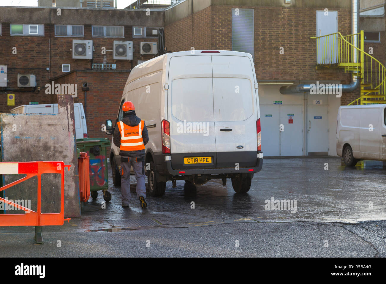 Homme avec une veste pontier-élingueur dirige une grande camionnette blanche dans l'entrée arrière d'un bâtiment, Ashford, Kent, UK Banque D'Images