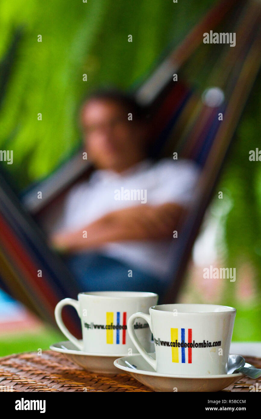La Colombie, Caldas, Manizales, Hacienda Venecia, tasses à café sur la table avec l'homme de vous détendre dans un hamac en arrière-plan Banque D'Images