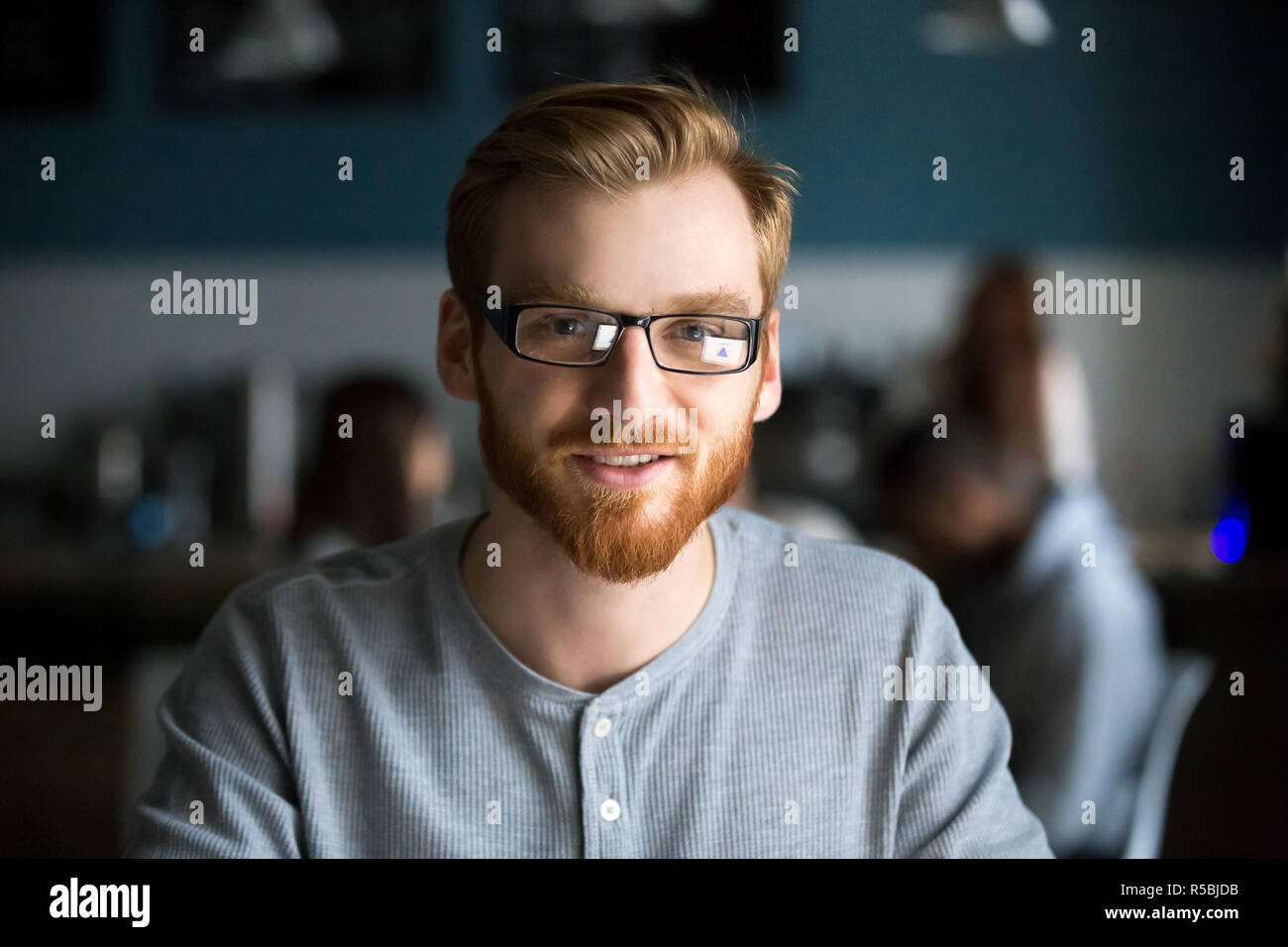 Portrait of smiling red haired millennial man looking at camera sitting in cafe ou coffeeshop, heureux jeune homme à lunettes qui pose pour photo travailler Banque D'Images