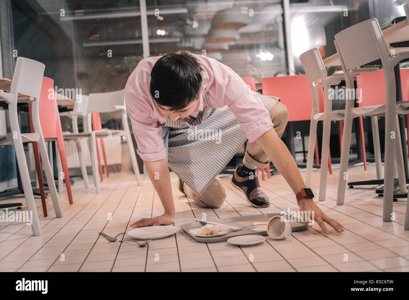Dark-haired waiter le nettoyage de la chaussée après avoir laissé tomber le bac avec de la nourriture Banque D'Images