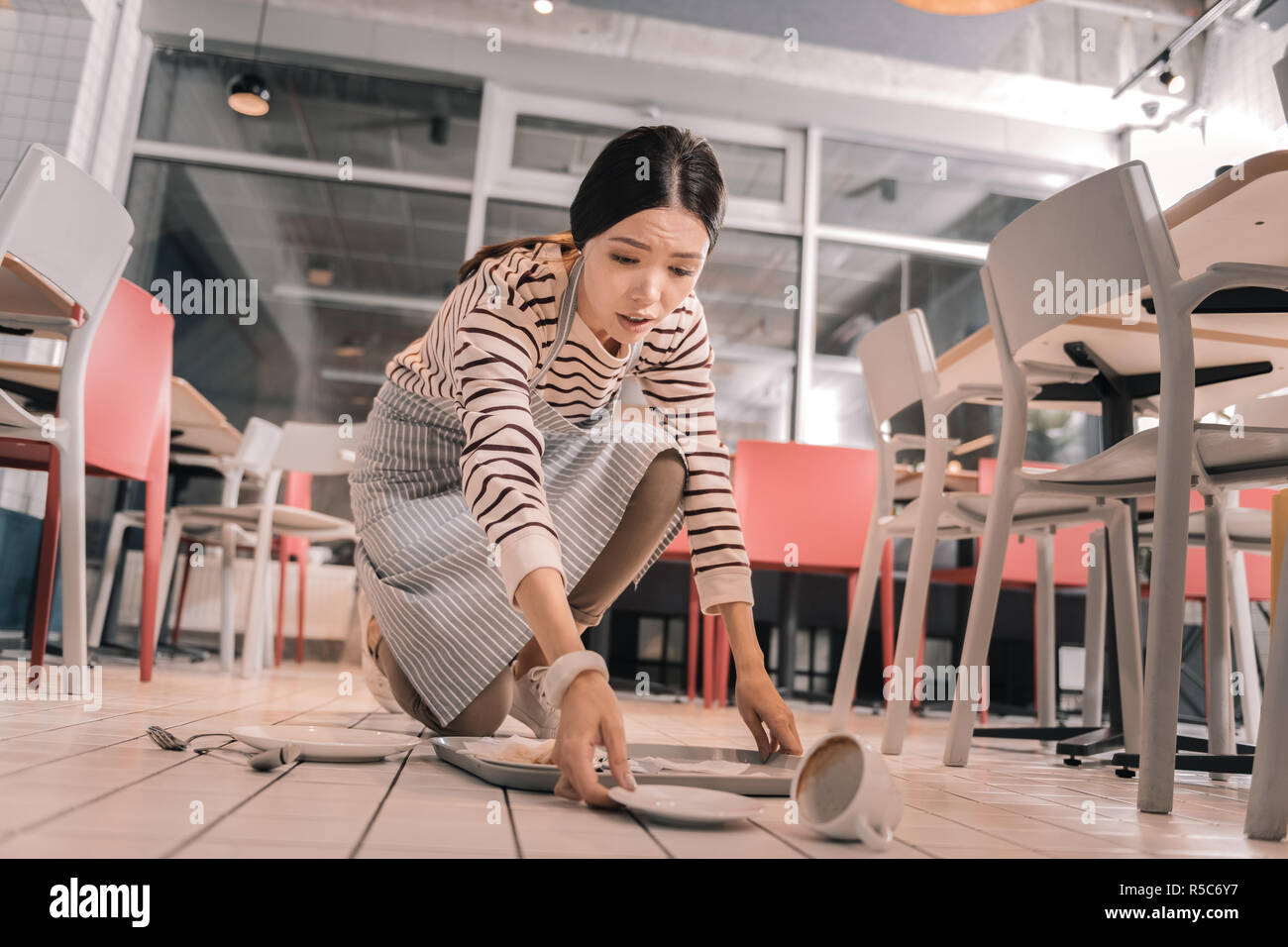 Jeune serveuse se sentir concerné après avoir laissé tomber le plateau avec de la nourriture Banque D'Images
