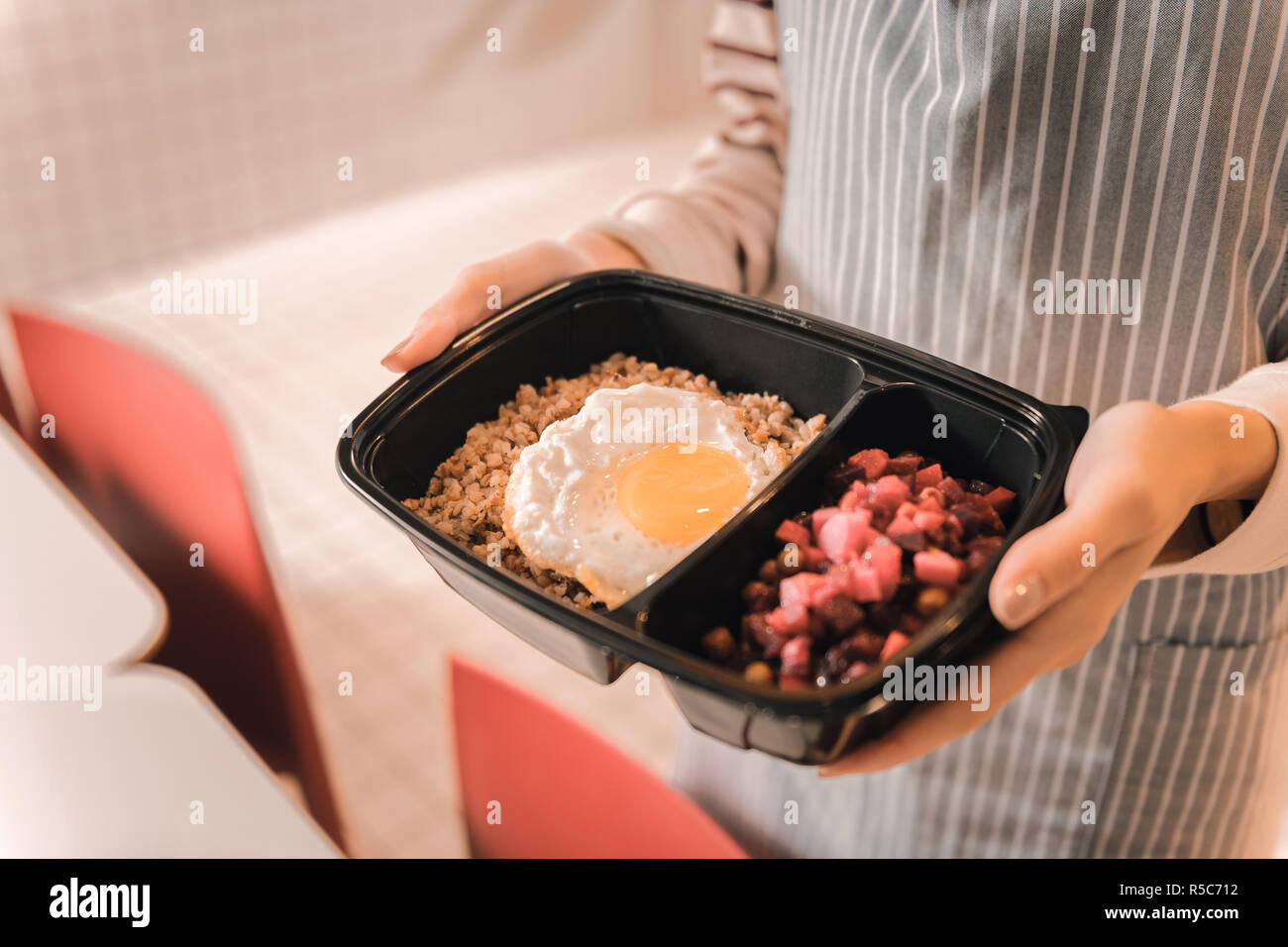 Jeune serveuse en tablier à rayures apportant le déjeuner fort pour le client Banque D'Images