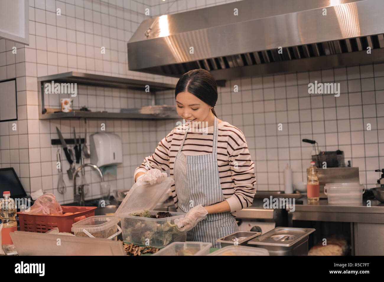 Dark-haired travailleur de la cuisine mettre la nourriture dans des contenants Banque D'Images
