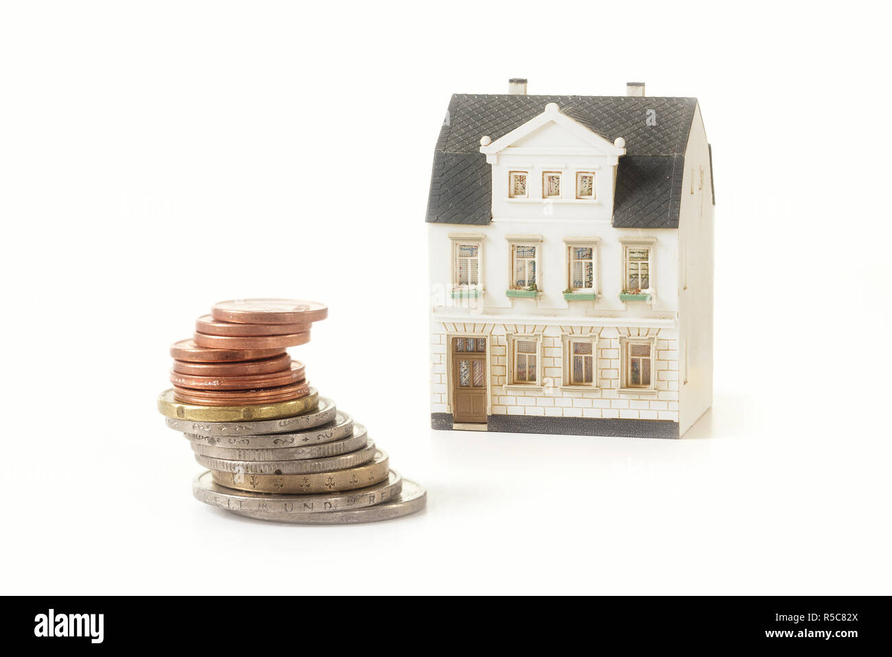 Pile de pièces à côté d'un vieux bâtiment miniature house, concept immobilier pour investissement de propriété ou de frais de location d'une maison isolée sur un bac blanc Banque D'Images