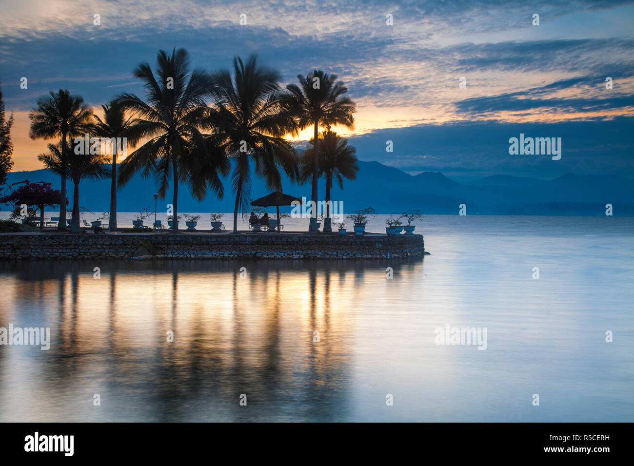 L'Indonésie, Sumatra, l'île de Samosir, Tuk Tuk, les gens assis sous plam arbres regardant le lever du soleil au Lac Toba Banque D'Images