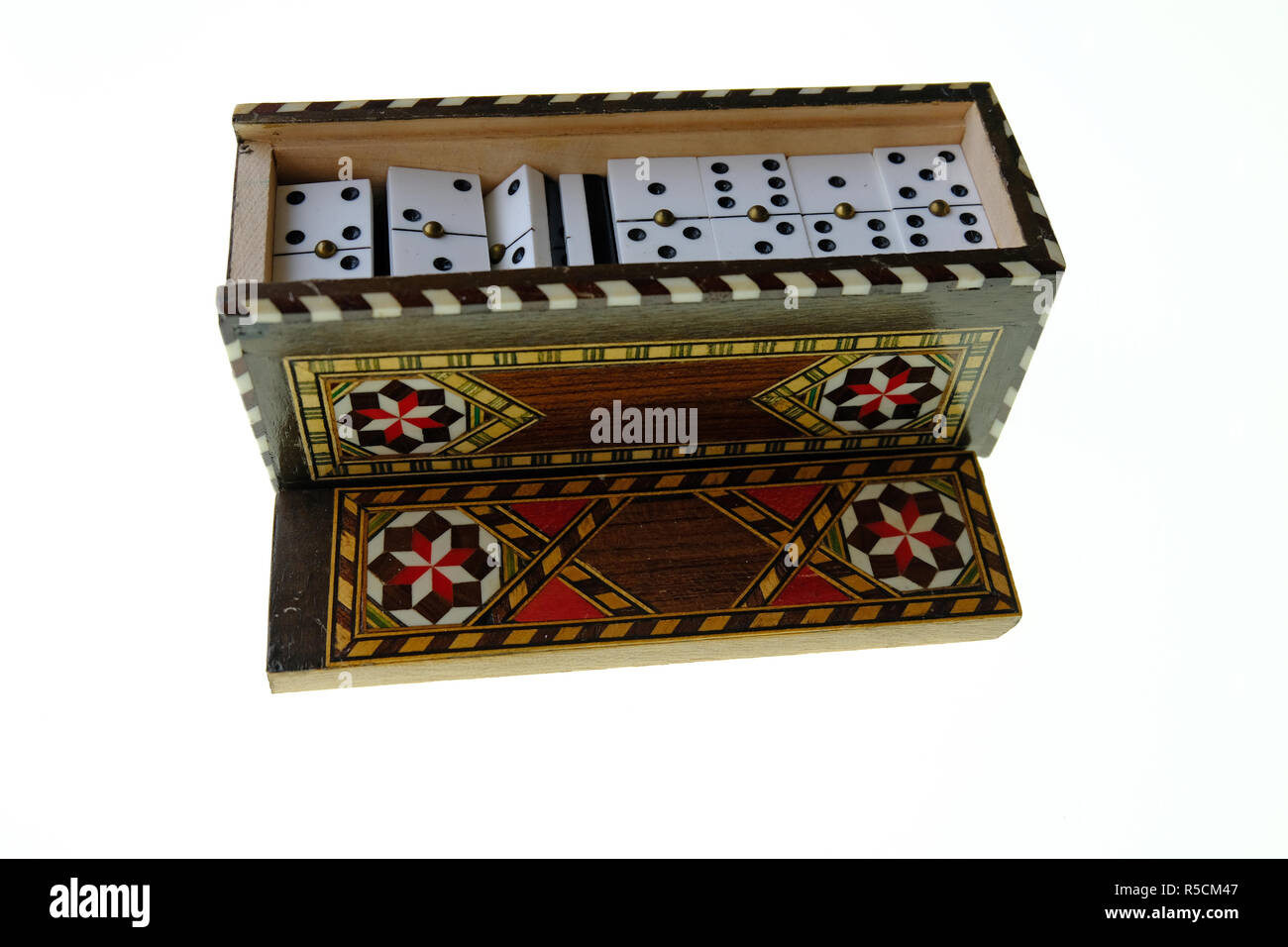 Petite boîte en bois avec couvercle coulissant marqueterie contenant un ensemble de petits dominos blancs avec des points noirs. Le tout sur un fond blanc Banque D'Images