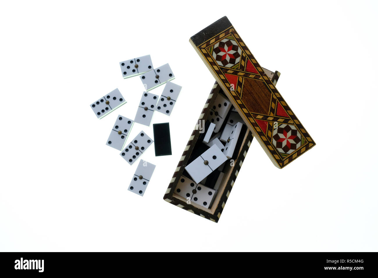 Petite boîte en bois avec couvercle coulissant marqueterie contenant un ensemble de petits dominos blancs avec des points noirs. Le tout sur un fond blanc Banque D'Images