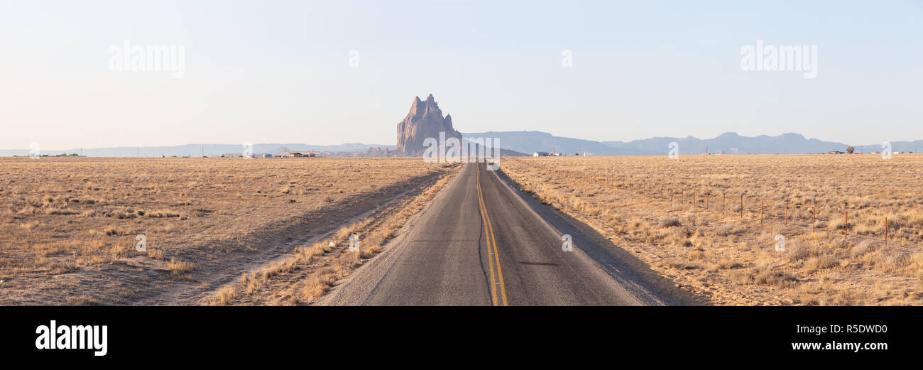 Vue panoramique d'une route dans un désert aride avec une crête de montagne de Shiprock en arrière-plan lors d'un lever de soleil vibrant.Prises au crotale, Nouveau Mexique Banque D'Images