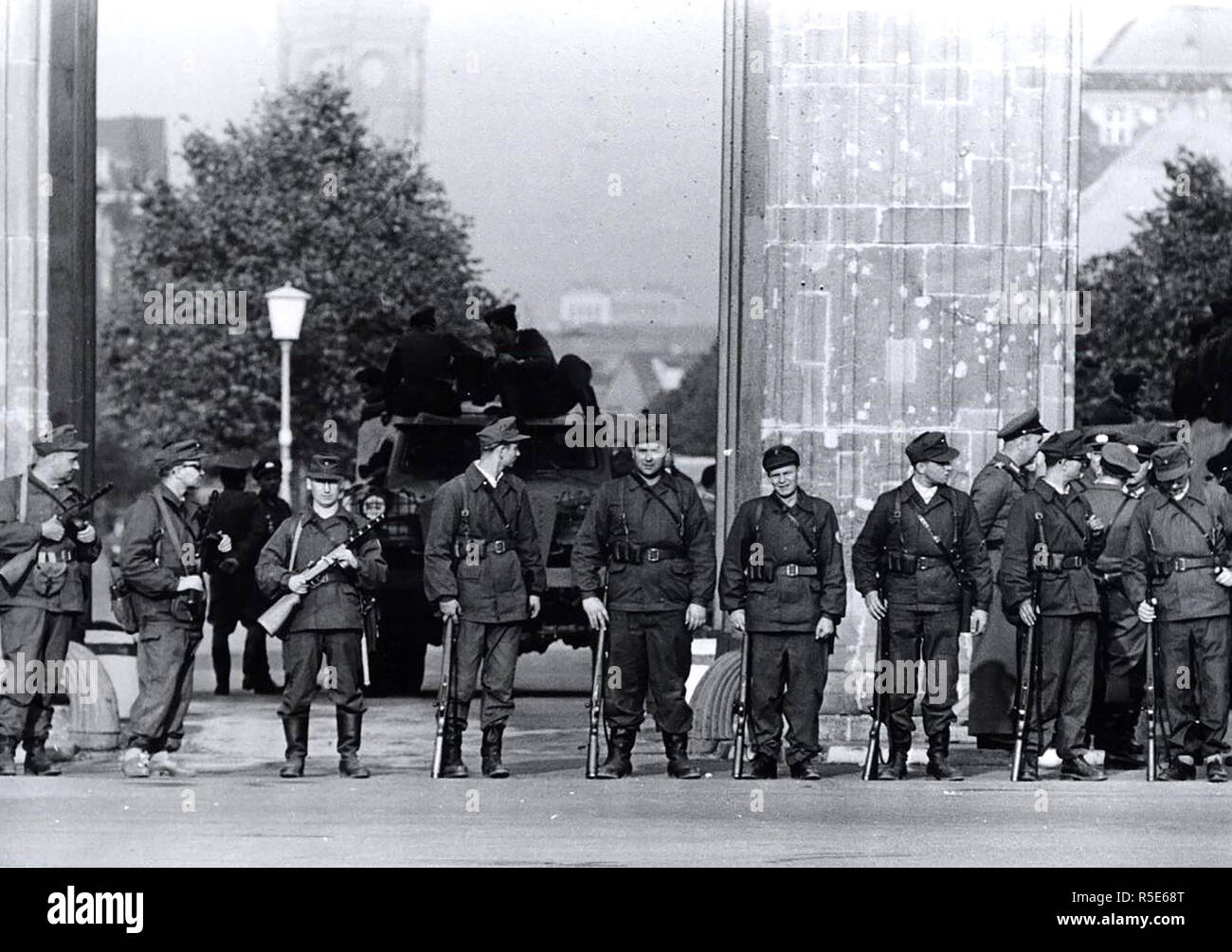 Août 1961 - une brigade de Berlin est "milice ouvrière' avec des mitraillettes s Shoulder-To-épaule devant la porte de Brandebourg. Derrière eux, bloquant le passage, est un communiste voiture blindée Banque D'Images