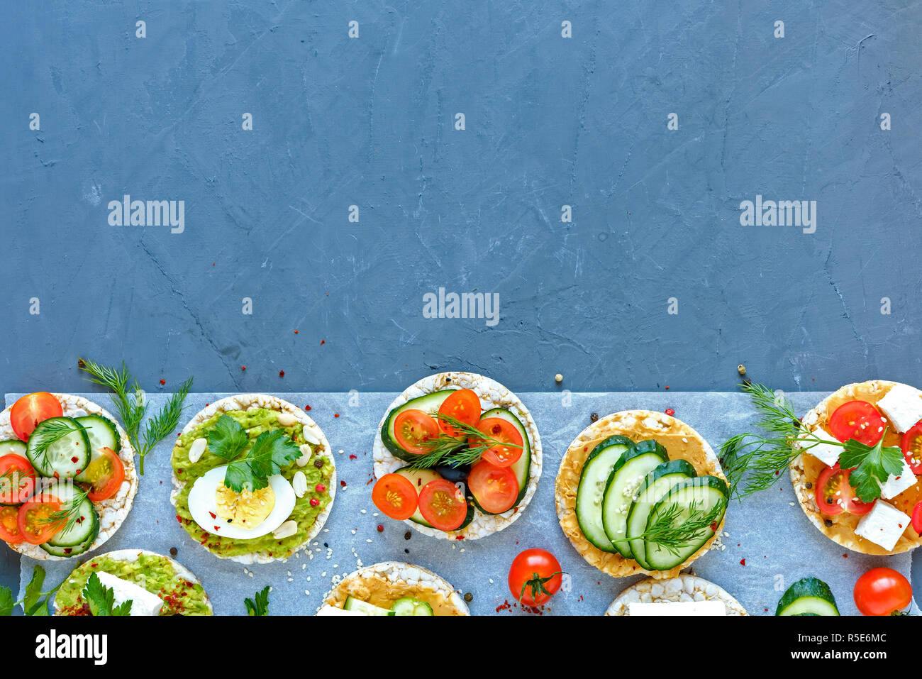 Border de savoureux amuse-gueules ou des canapés avec des légumes frais, fromage feta et d'oeufs sur les gâteaux de riz organisé sur blue with copy space Banque D'Images