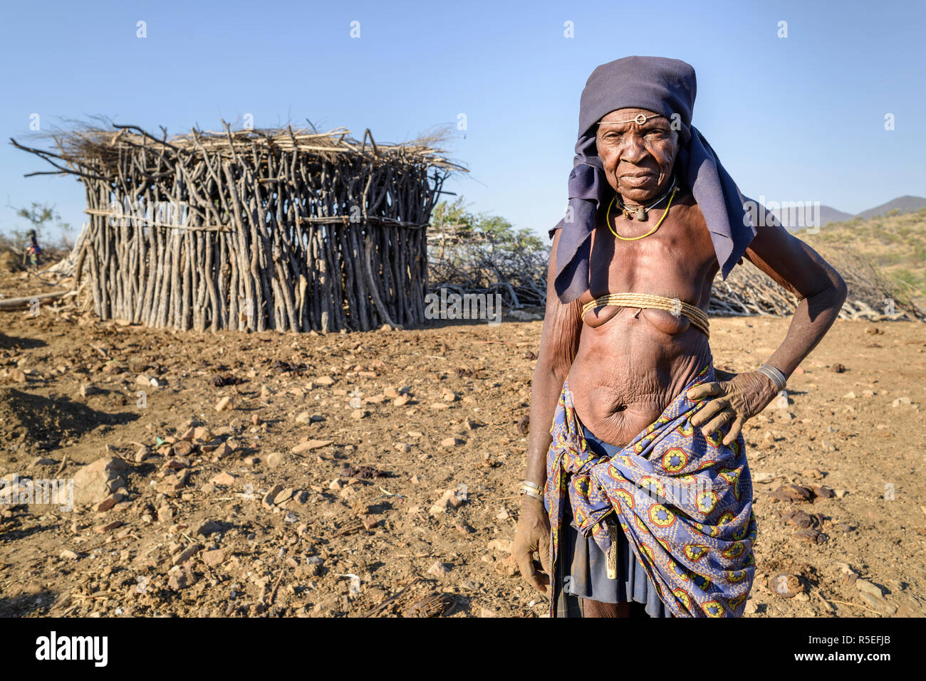 Portrait d'une vieille femme Mucubale avec laiton traditionnel devant sa hutte. Banque D'Images
