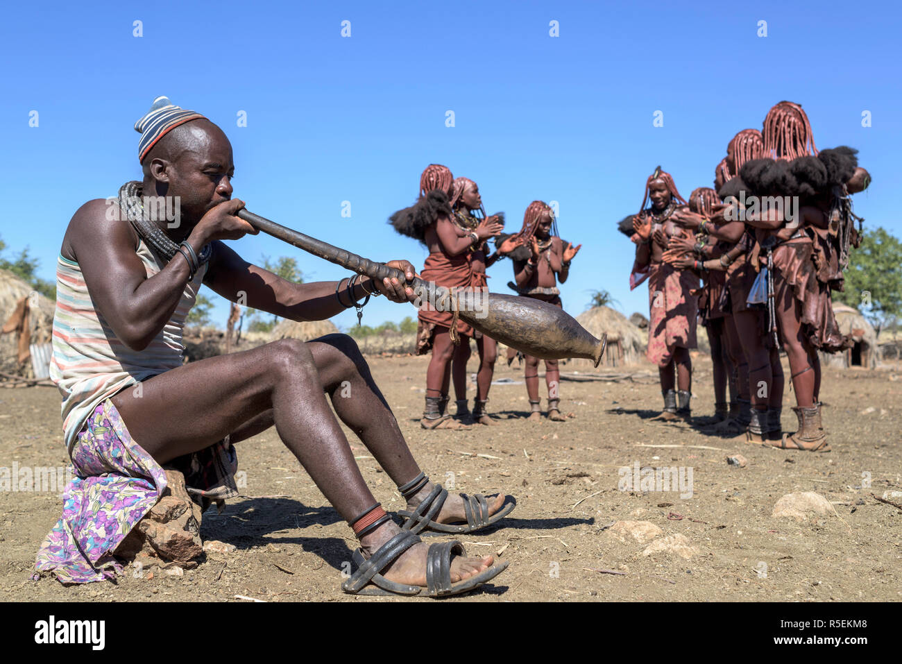 Groupe des femmes Himba avec costumes traditionnels de danser dans un cercle alors qu'un homme joue un violon fabriqué à partir d'une corne orix. Banque D'Images