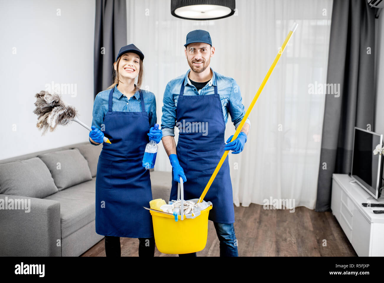 Portrait d'un jeune couple comme les nettoyeurs professionnels en uniforme bleu avec des outils de nettoyage dans l'appartement Banque D'Images