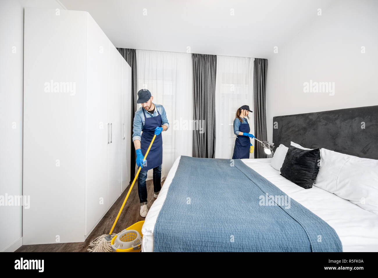 Les nettoyeurs professionnels en uniforme lave-de-chaussée et d'essuyer la poussière sur les meubles dans la chambre d'hôtel ou un appartement une chambre. Le concept de service de nettoyage Banque D'Images