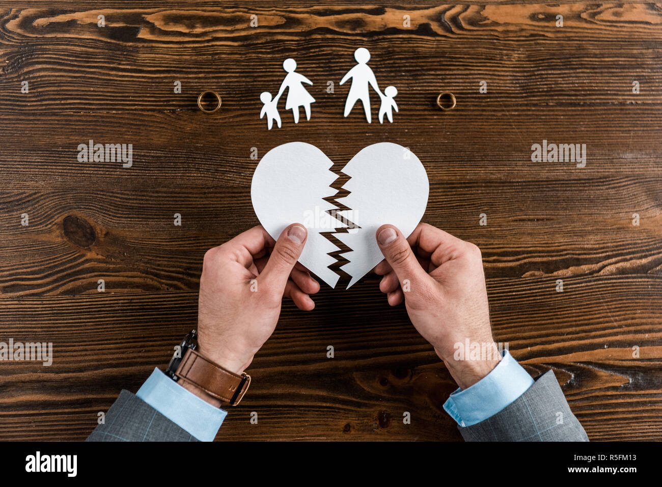Cropped shot of man holding a coeur avec la famille et des anneaux d'enclenchement sur table en bois, concept de divorce Banque D'Images