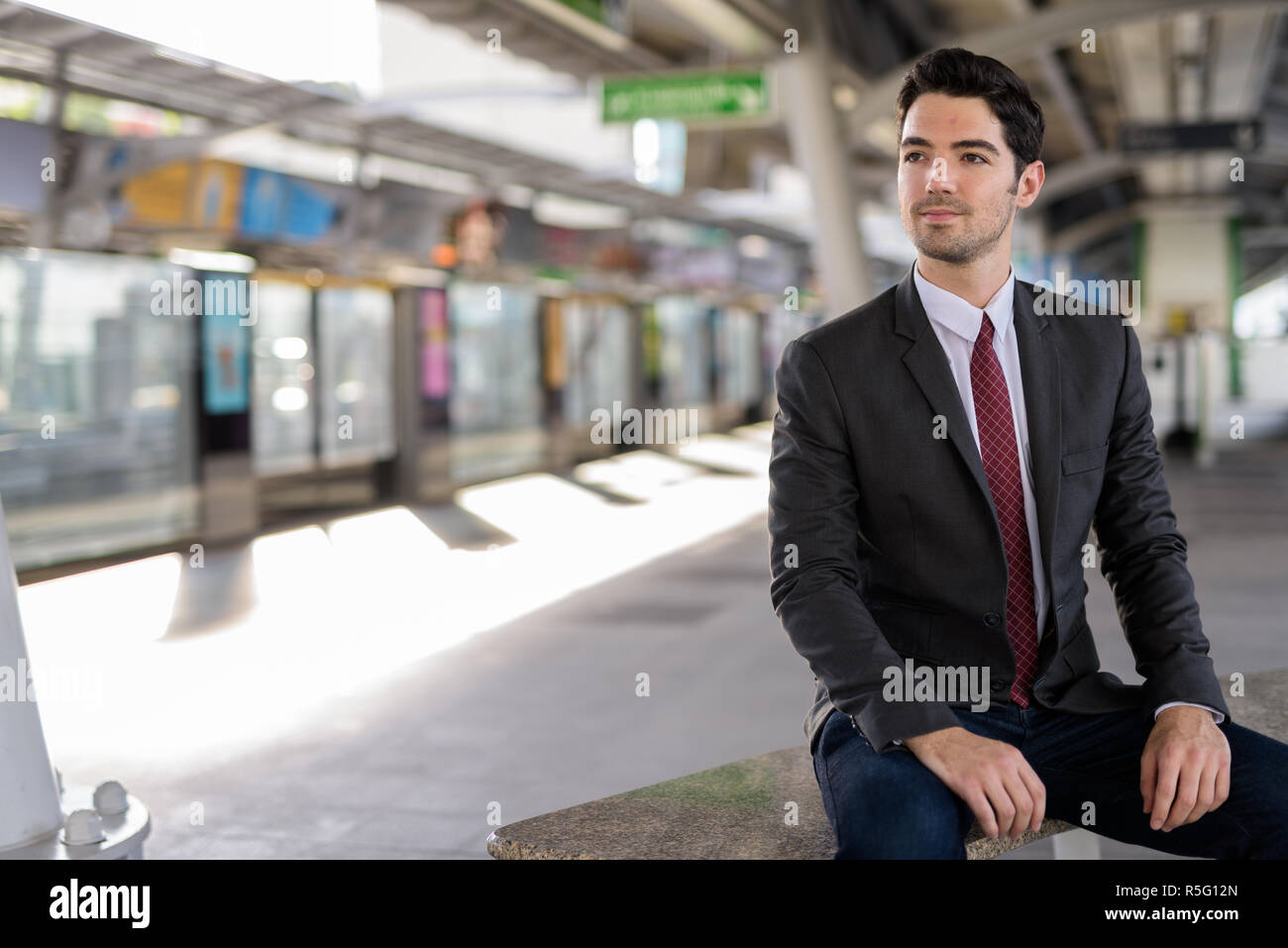 Portrait of young handsome businessman sitting at train station Banque D'Images