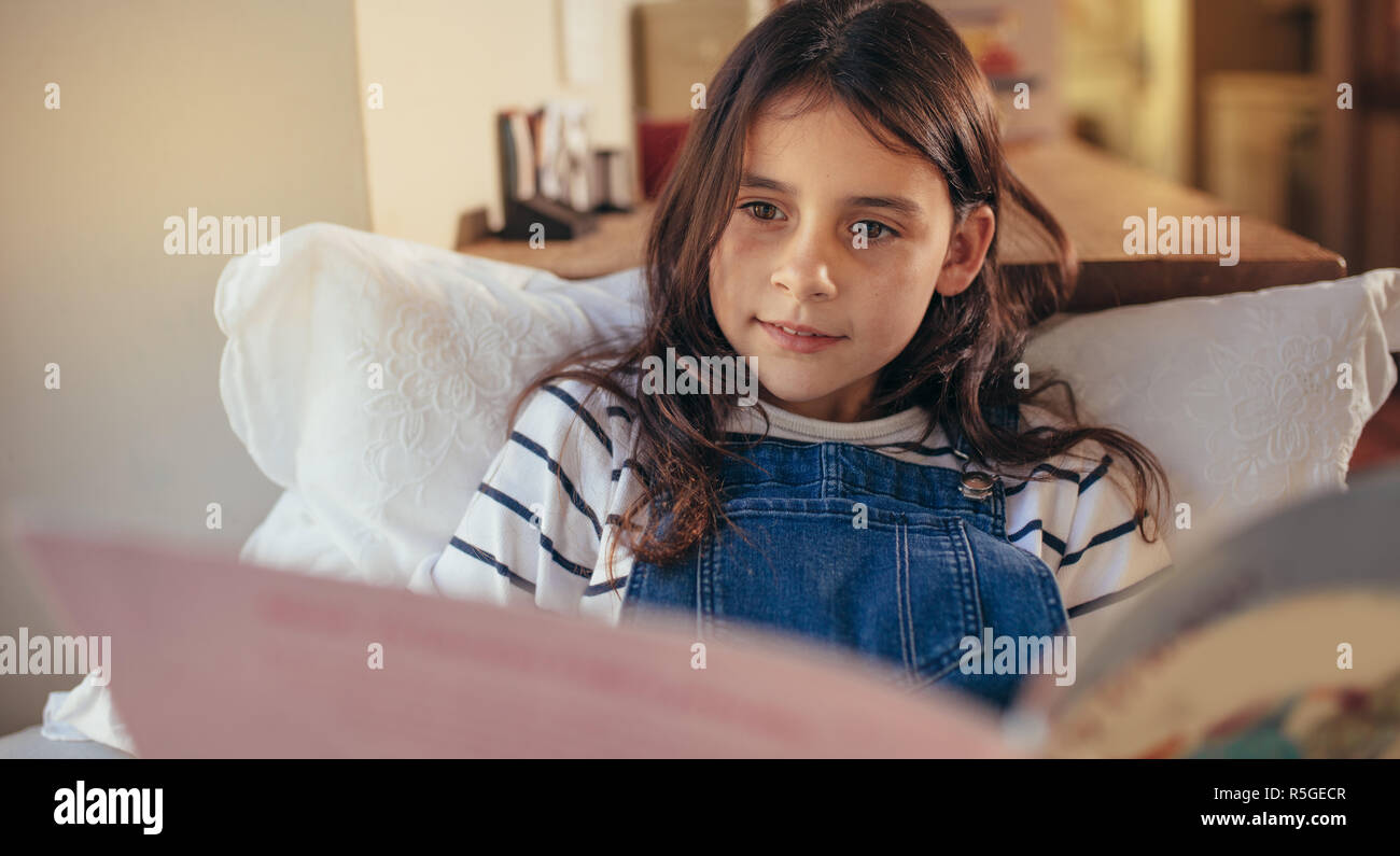 Jeune fille assise à la maison Lire un livre. Cute caucasian girl élève plongé dans la lecture de livre d'histoires à l'intérieur. Banque D'Images