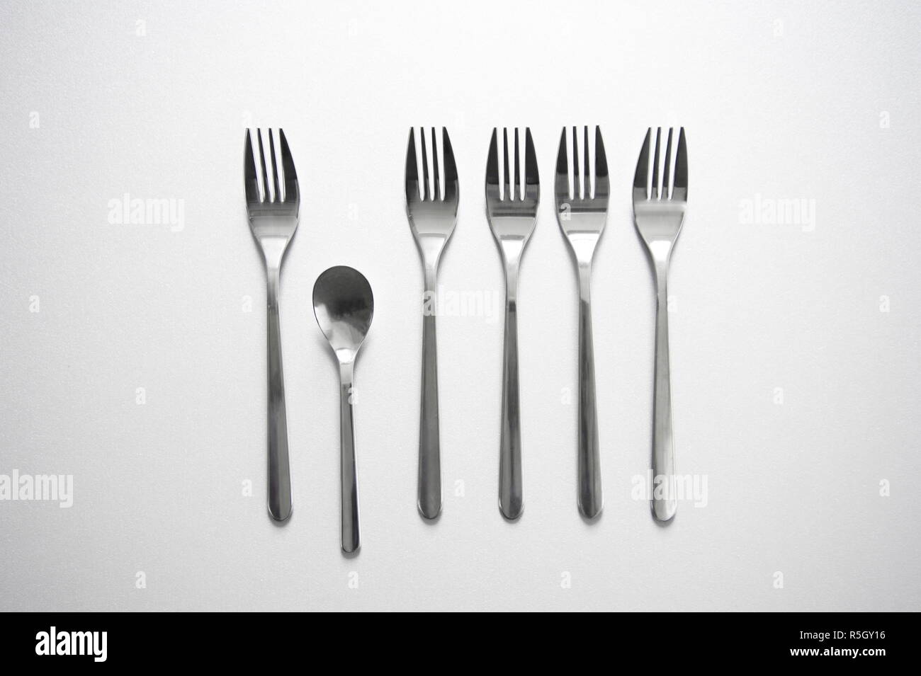 Rangée de fourche en métal argenté avec petite cuillère unique sur fond gris photo conceptuelle de la concurrence ou de l'alimentation arrière-plan d'affaires Banque D'Images