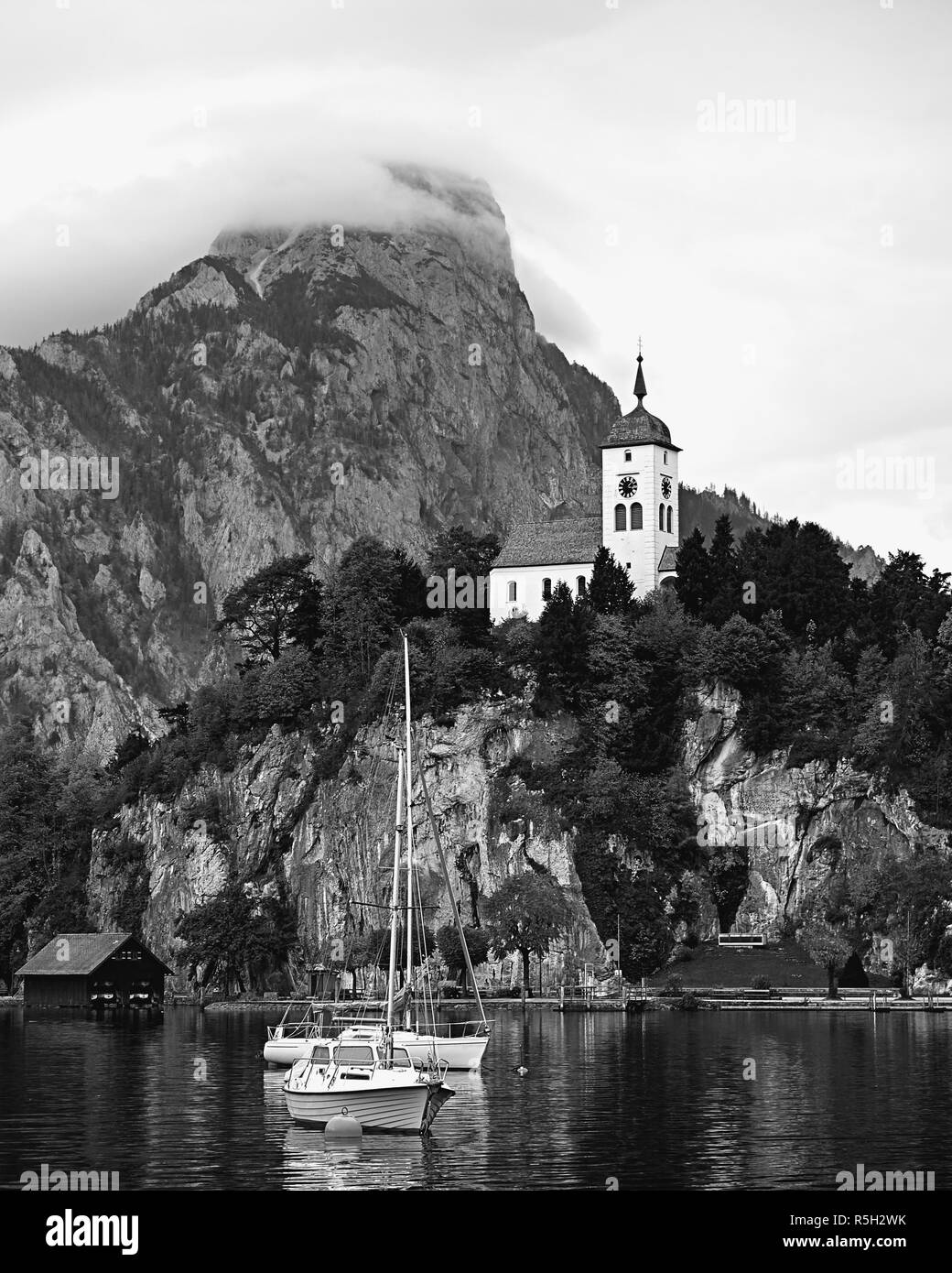 Vintage noir et blanc vue sur lac Alpes autrichiennes. Bateaux, yachts en face de l'église sur le rocher avec des nuages sur les Alpes montagne à Traunstein lake Banque D'Images