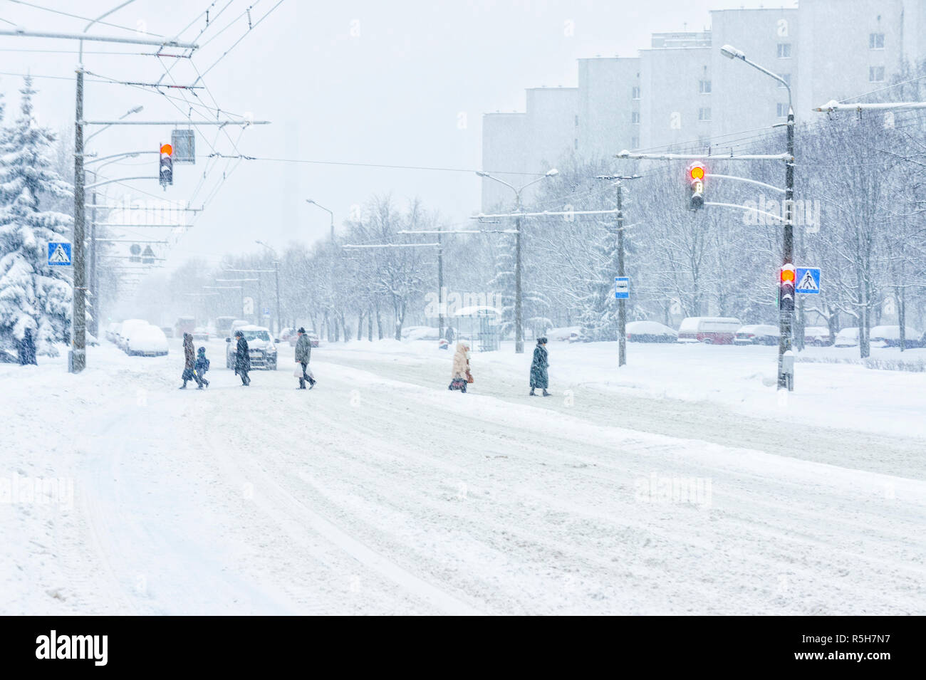 Passage pour piétons lors d'une tempête de neige. Silhouettes de personnes traversant la chaussée recouverte d'une épaisse couche de neige. Concept de ville d'hiver Banque D'Images