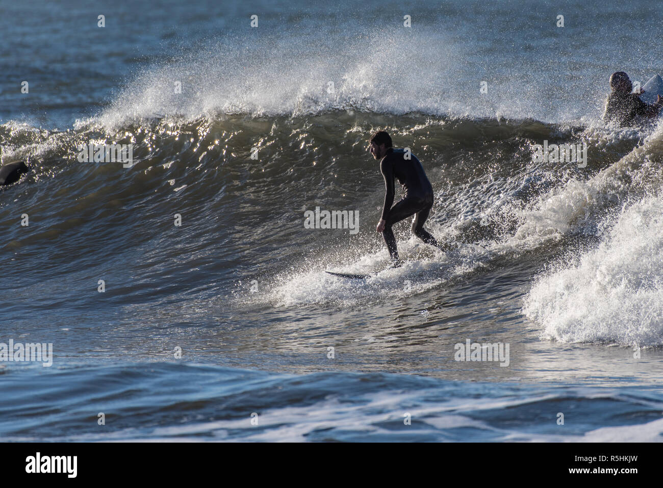 Surfer barbu en combinaison noire montrant la posture classique comme il tombe dans l'éolien offshore ensemble soufflé vague dans Ventura, Californie, USA le 1 décembre 2018. Banque D'Images