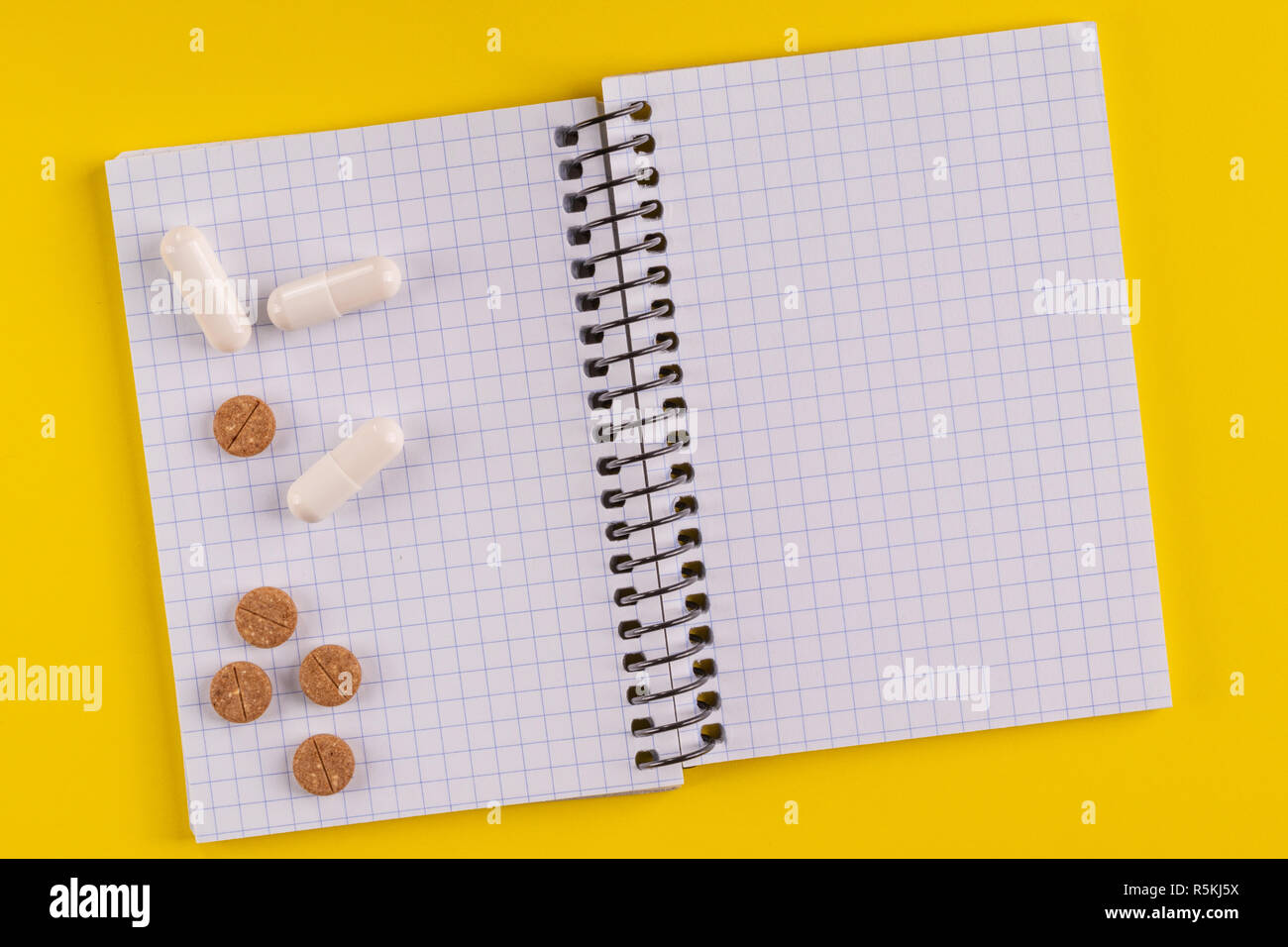 Medical capsules et comprimés autour d'un bloc-notes en blanc sur un fond jaune, close-up, vue du dessus, avec l'exemplaire de l'espace. Banque D'Images