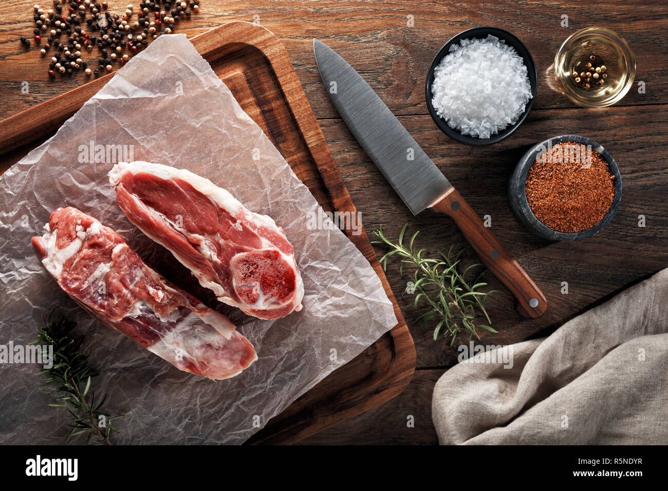 Ragoût d'agneau cru blanc sur papier de cuisson et planche à découper en bois. Décorées avec des herbes, épices et couteau de chef. Vue de dessus. Banque D'Images