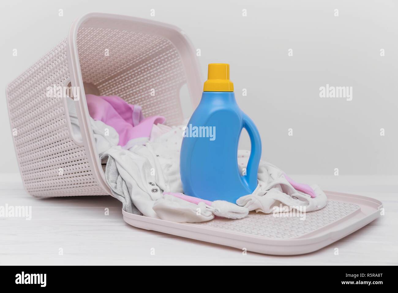 Bouteille de lessive dans le panier avec des vêtements de bébé. Banque D'Images