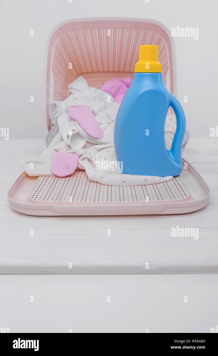 Bouteille de lessive dans le panier avec des vêtements de bébé. Banque D'Images