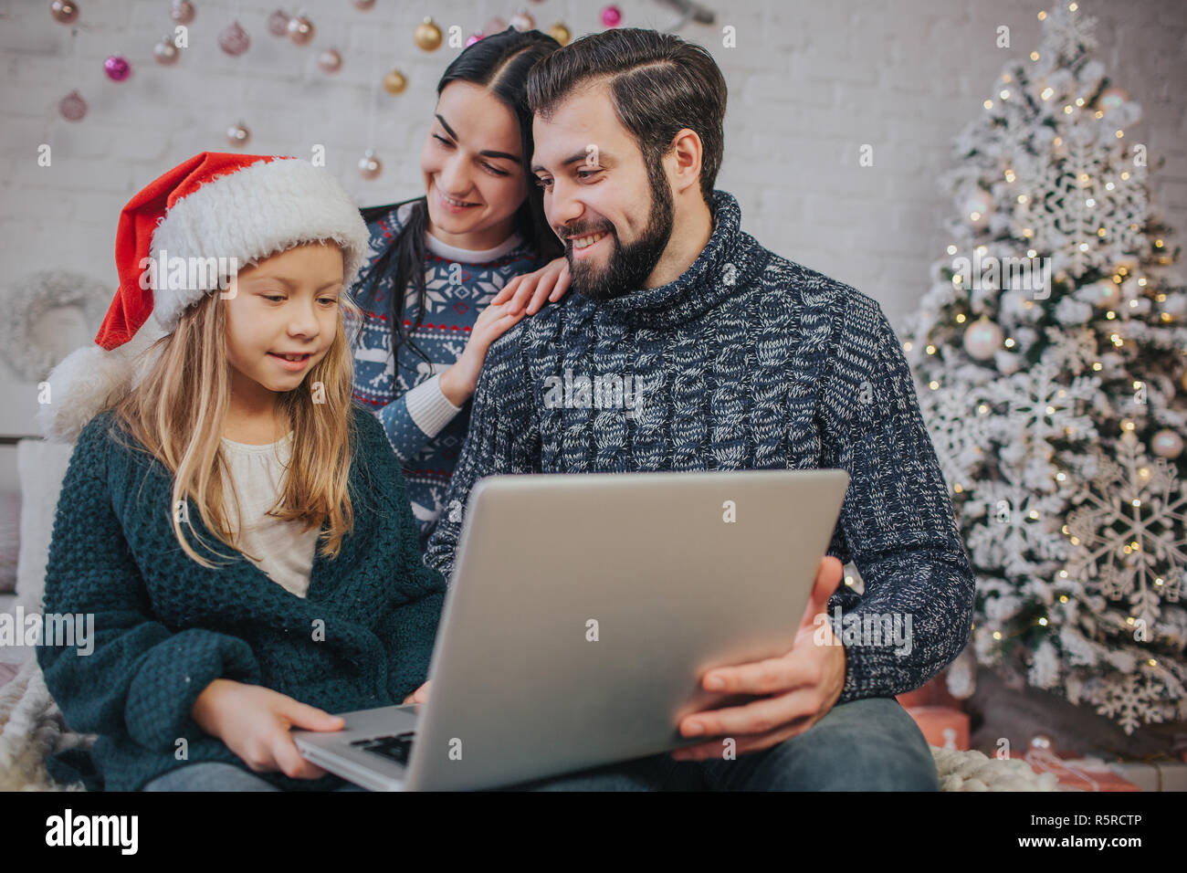 Joyeux Noël et de bonnes vacances joyeux maman, papa et sa fille cute girl d'utiliser un ordinateur portable. Parent et enfant s'amusant près de l'arbre de Noël à l'intérieur. Matin Noël. Famille Portrait close up. Shopping en ligne de chaleureux séjour à la maison. Banque D'Images