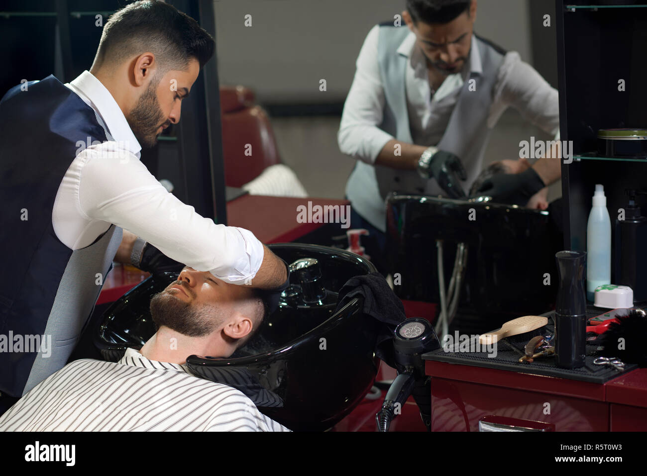 Coiffure élégante en chemise blanche, gilet et de gants de lavage des cheveux de clients masculins avant de couper et de style dans un salon de coiffure. Concept de l'opération de lavage et la coiffure. Banque D'Images
