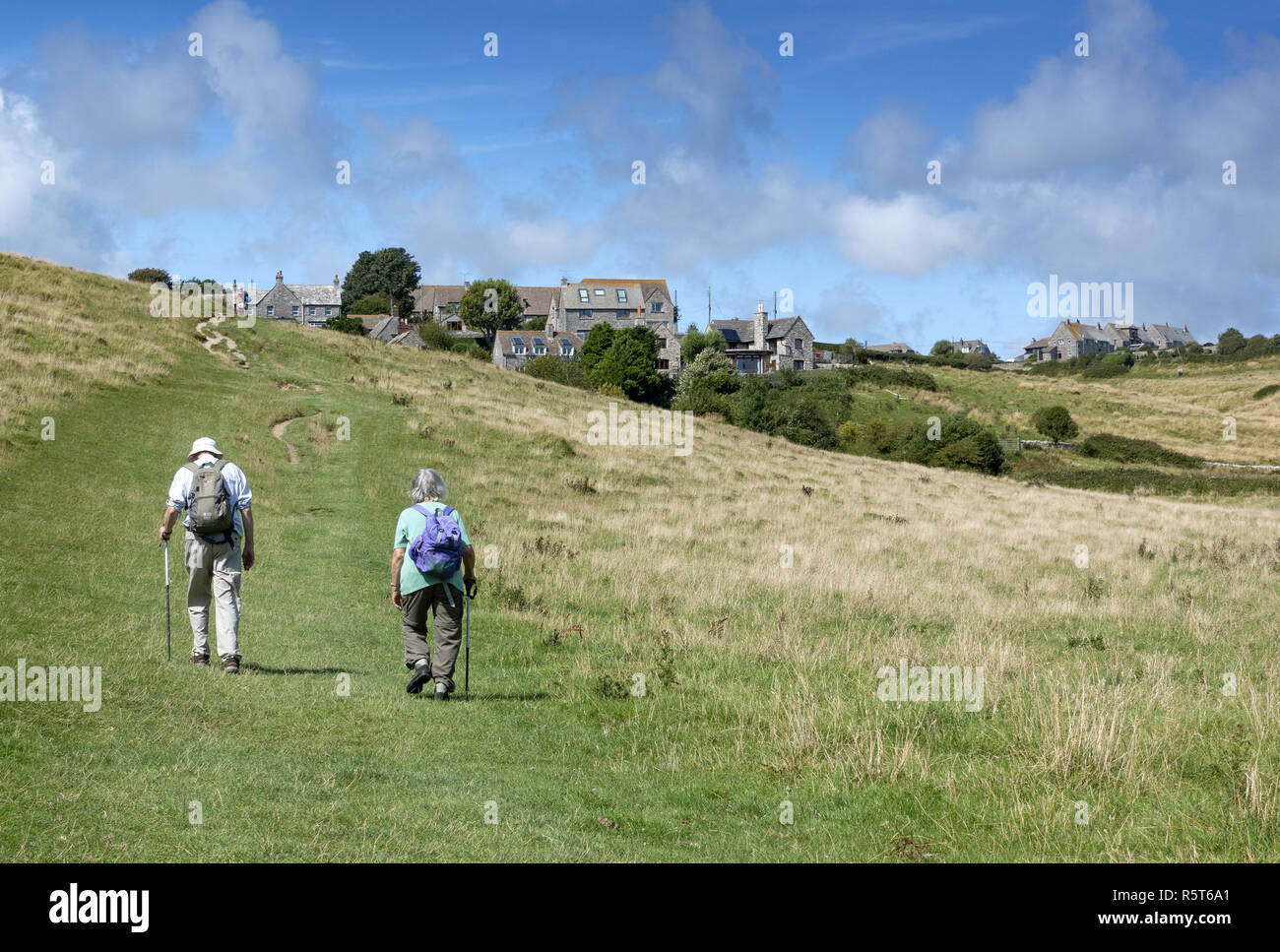 Couple de personnes âgées avec sacs à dos en direction du village pittoresque de Worth Matravers sur l'île de Purbeck, Dorset, Angleterre, Royaume-Uni Banque D'Images