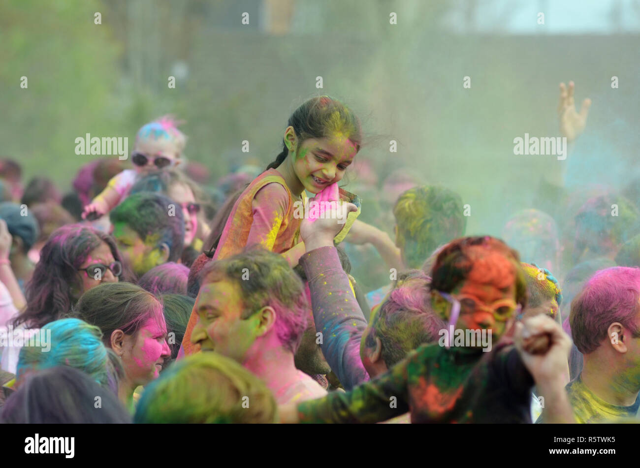Un homme touche un visage de la fille comme elle se trouve au-dessus des épaules de ses parents lors d'une célébration de Holi, la fête hindoue des couleurs, à Redmond, Washington Banque D'Images