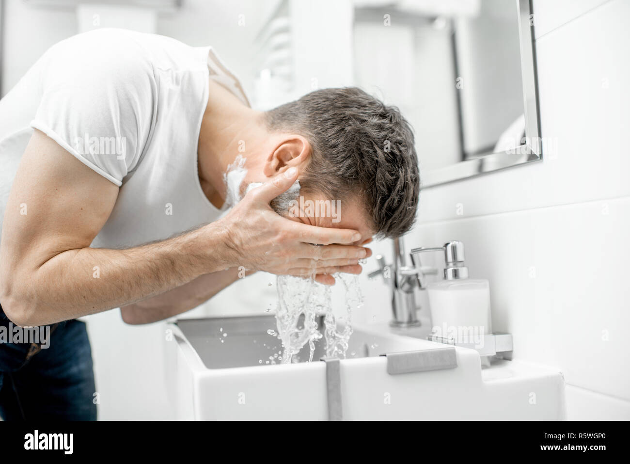 L'homme lave son visage avec de l'eau fraîche et de la mousse dans l'évier à la salle blanche Banque D'Images