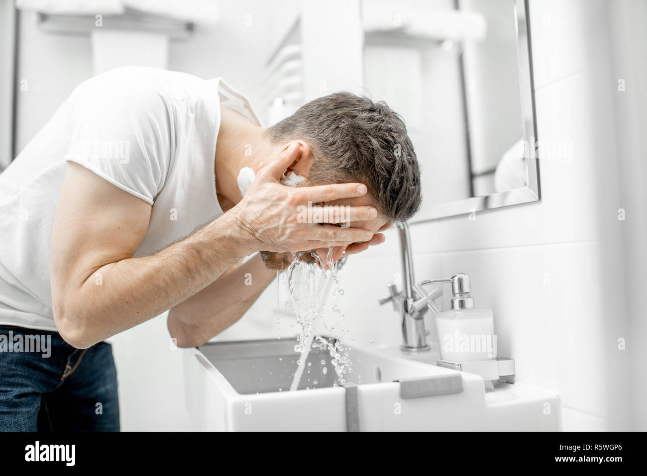 L'homme lave son visage avec de l'eau fraîche et de la mousse dans l'évier à la salle blanche Banque D'Images