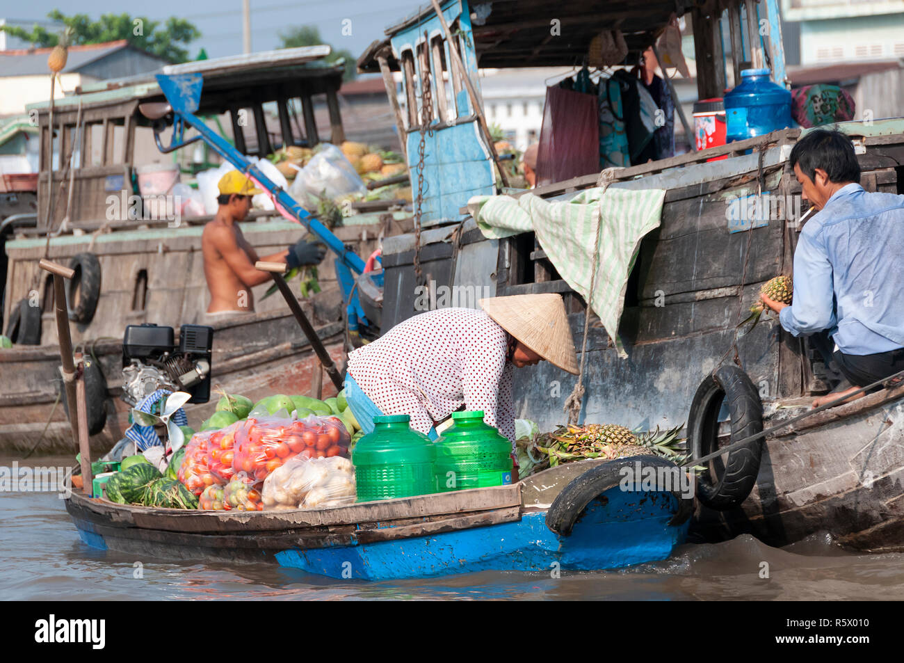 Boatwoman femelle vente des produits mains sur un ananas à un acheteur sur un autre bateau en bois au marché flottant de Cai Rang, Province de Can Tho, Vietnam Banque D'Images