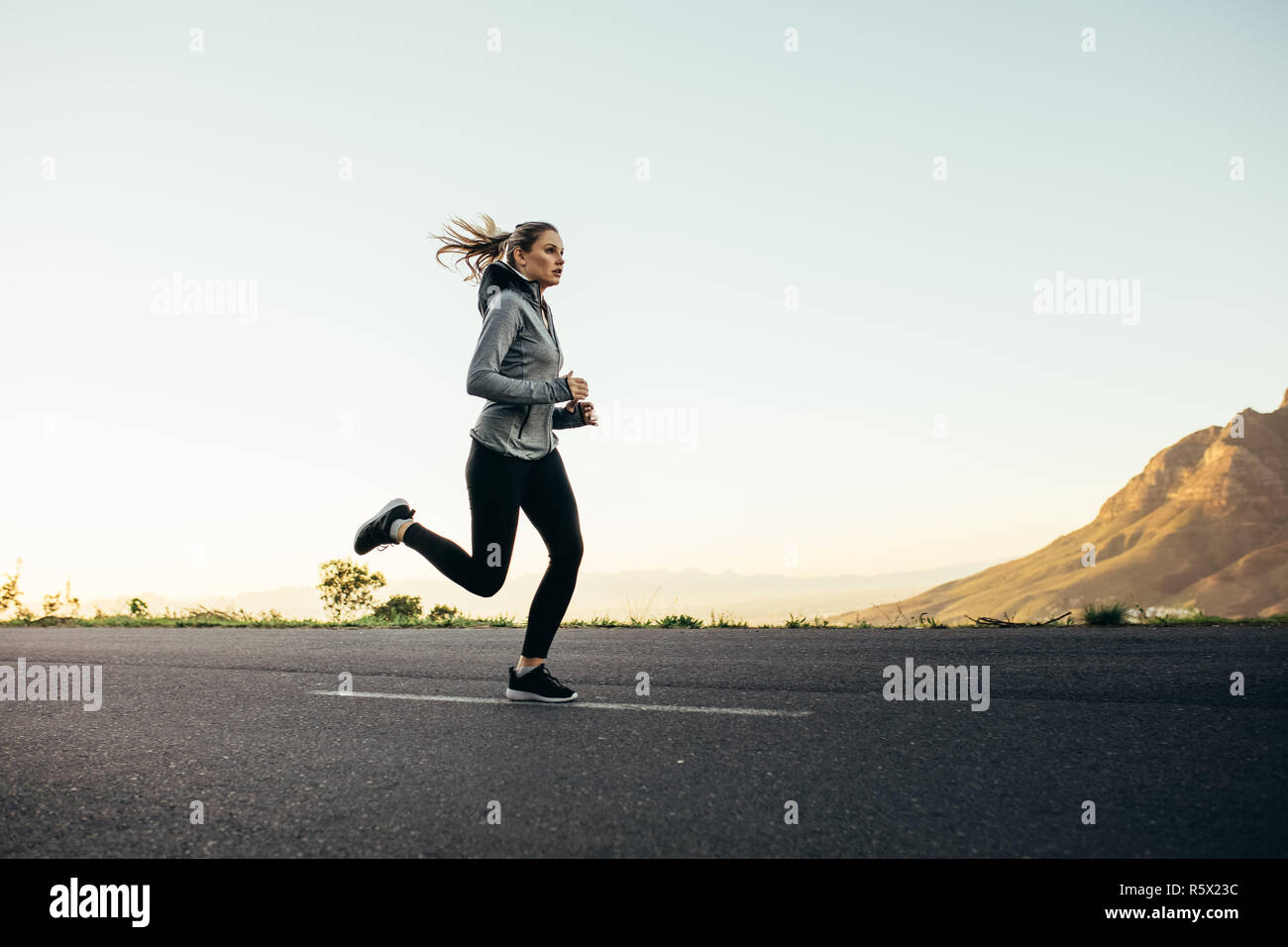 Athlète femme Running on Empty road. Vue latérale d'une femme de remise en forme sprint sur route. Banque D'Images