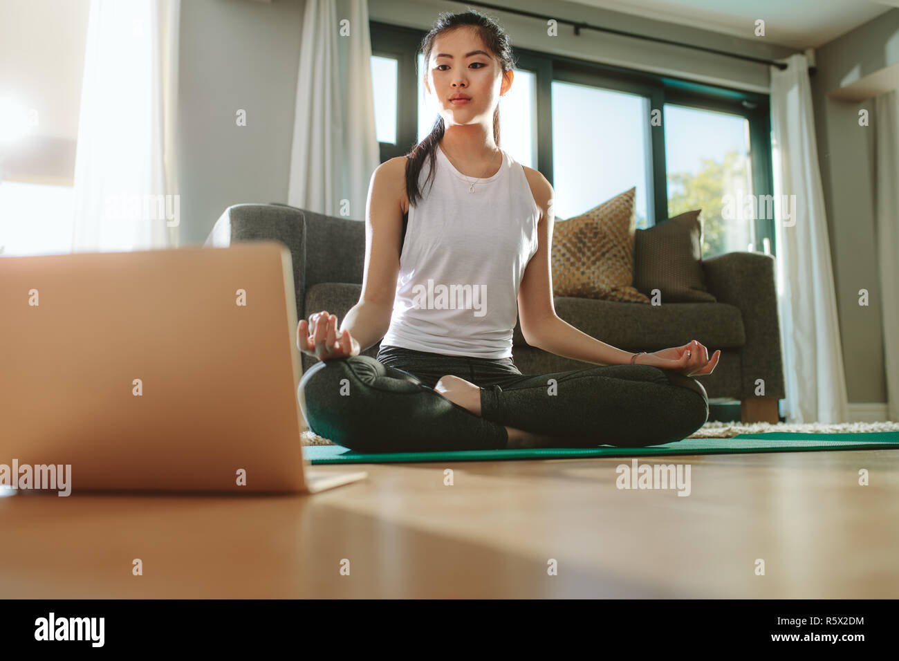 Belle femme chinoise l'exercice de yoga tout en regardant des vidéos sur ordinateur portable. Fit woman watching tutoriel sur l'ordinateur portable à la maison et faire du yoga ne Banque D'Images